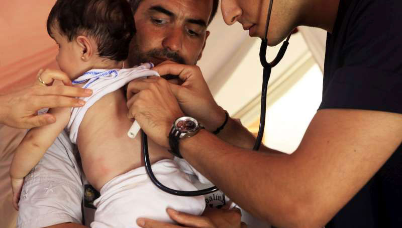 pai sírio observa enquanto um turco da equipe médica examina sua filha, que desenvolveu dificuldades na respiração. Foto: ACNUR/A.Branthwaite.